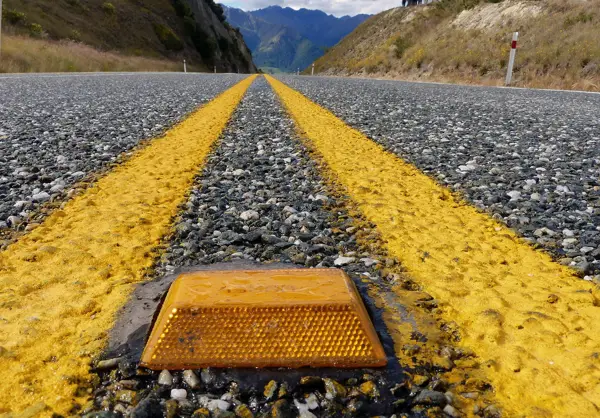 A cat’s eye road stud set between two yellow lines on a mountain road