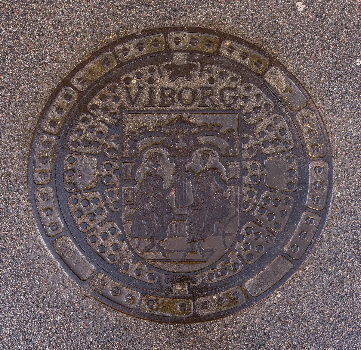 A round cast-iron manhole cover set in a pavement in Viborg, Denmark