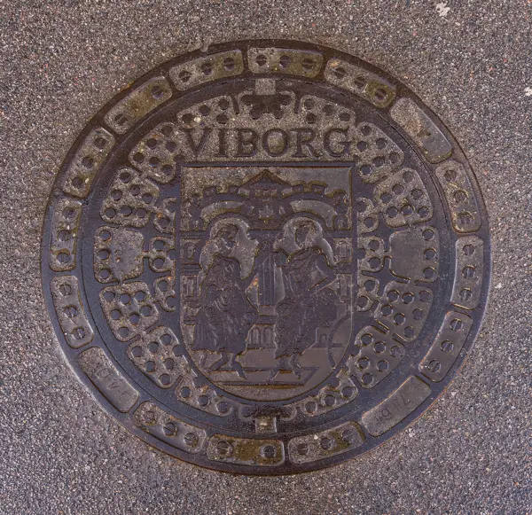 A round cast-iron manhole cover set in a pavement in Viborg, Denmark